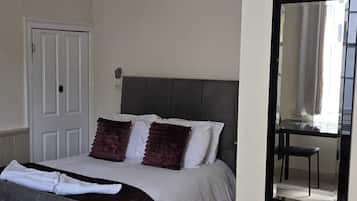 A bedroom with a bed, a chair, a door, and a mirror on the wall.