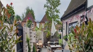 An outdoor patio area with multiple tables and chairs, surrounded by potted plants and a brick wall. - The White Hart Hotel (St Albans)