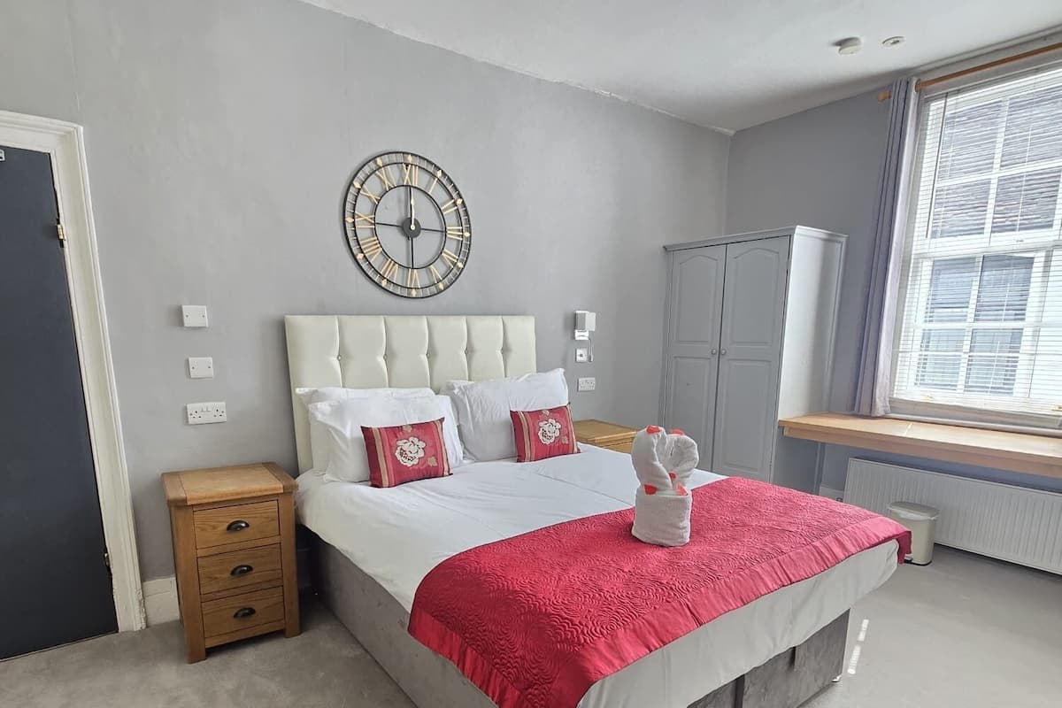 Une chambre à coucher avec un lit, des tables de chevet, une horloge, une armoire et une fenêtre.