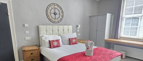 A bedroom with a bed, bedside tables, a clock, a wardrobe, and a window.