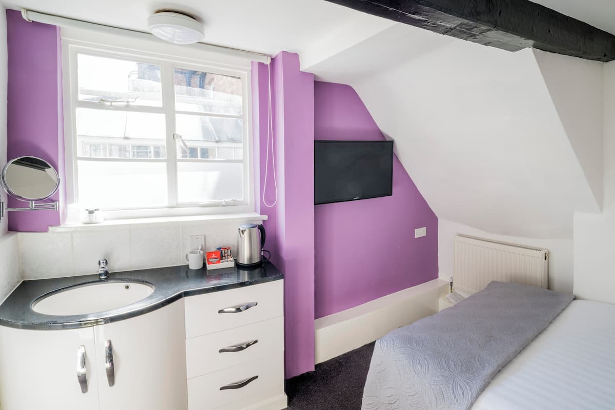 Une chambre à coucher avec un lit, une fenêtre, un lavabo et un téléviseur fixé au mur.