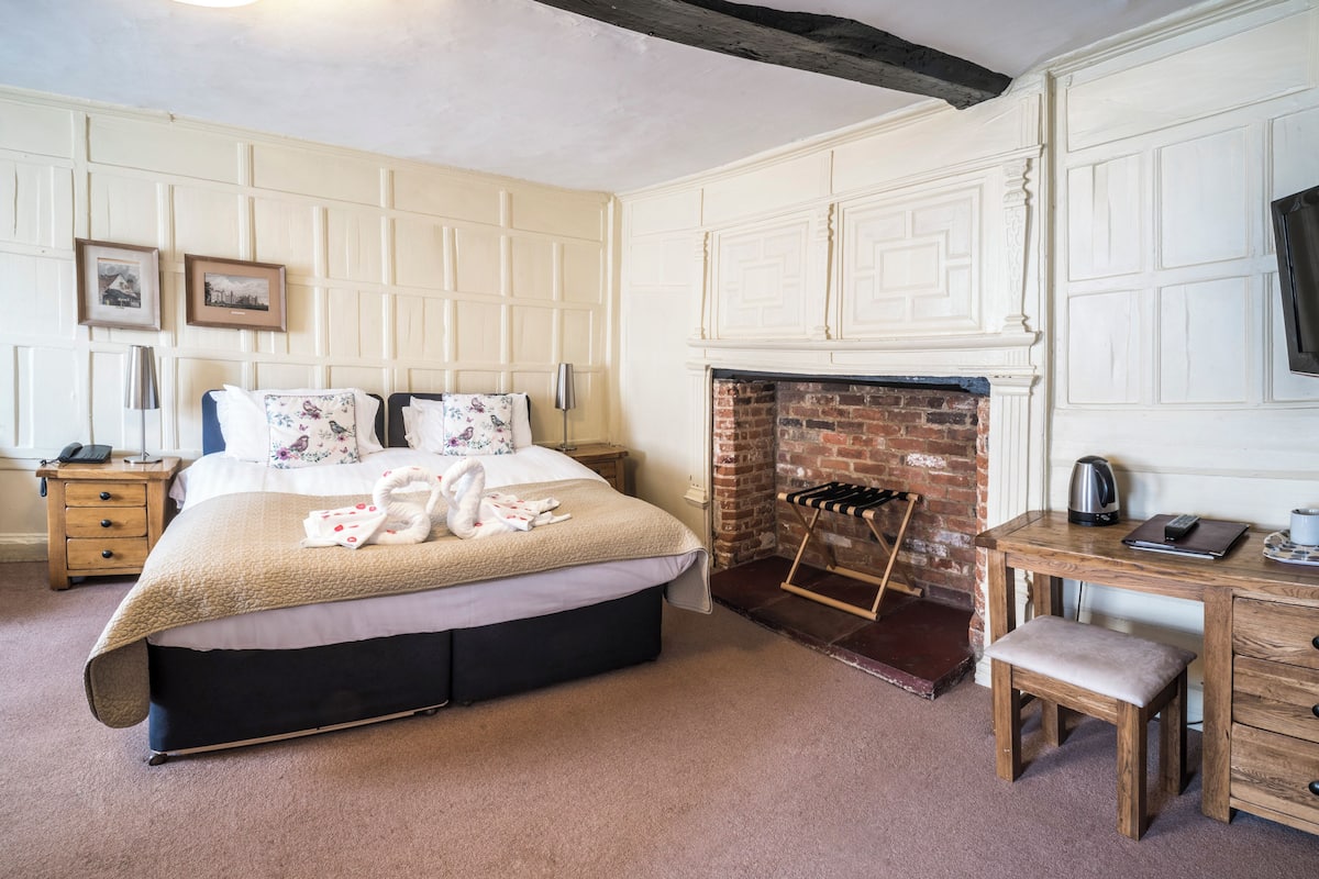 Une chambre à coucher avec un lit, un bureau en bois, une cheminée et une table de chevet.