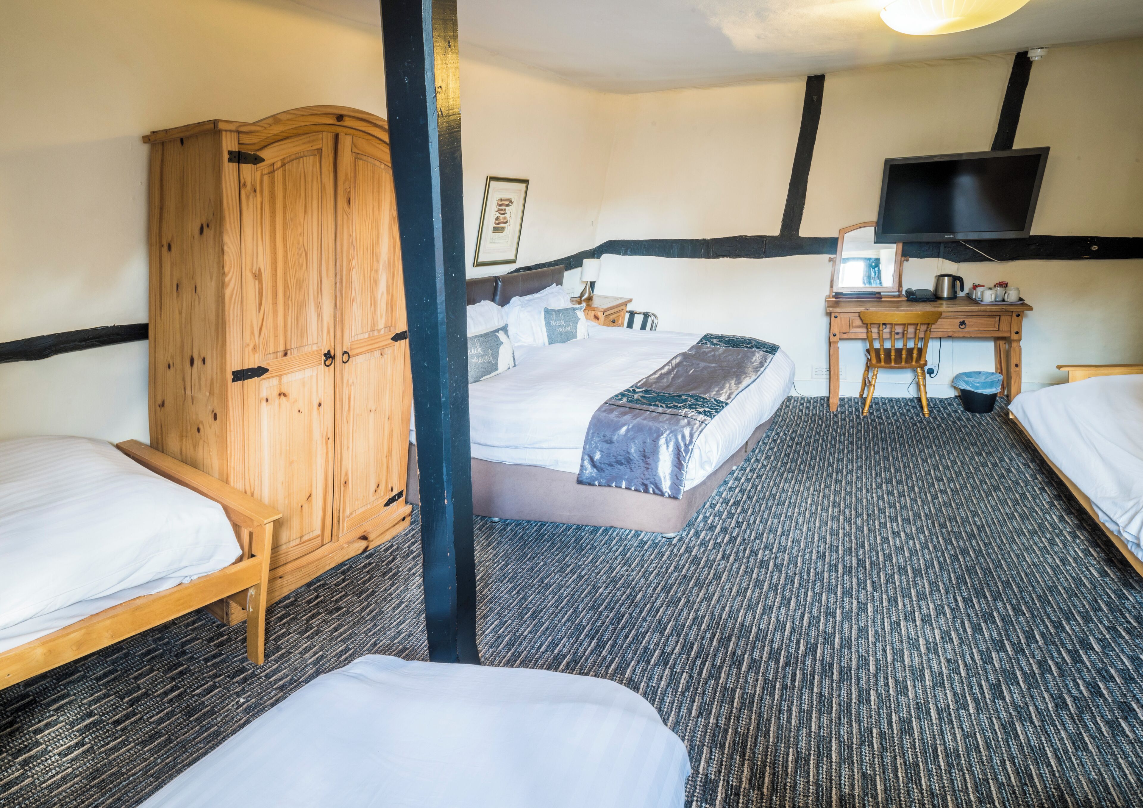A hotel room with a bed, a desk, a chair, a wardrobe, and a television.