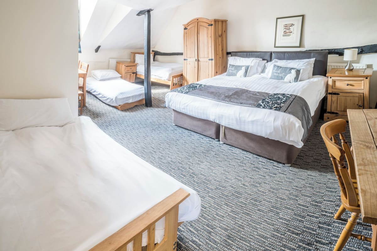 Une chambre d’hôtel avec un grand lit, un lit plus petit, un bureau, une chaise, une armoire et un tableau encadré au mur.
