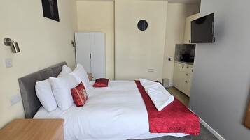 A bedroom with a bed, a wardrobe, a TV, and a clock on the wall.