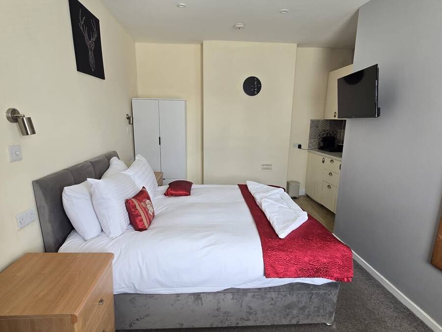 A bedroom with a bed, a wardrobe, a TV, and a clock on the wall.