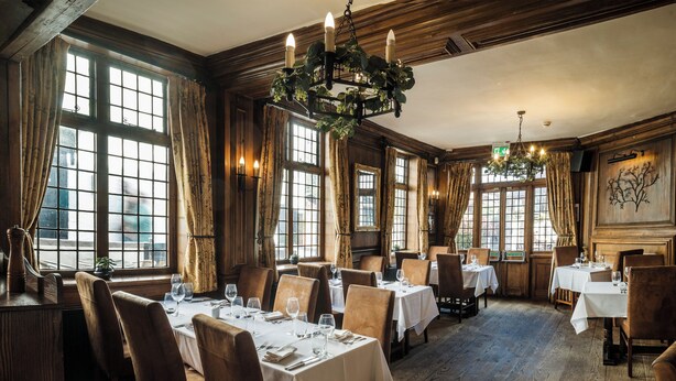 A restaurant with multiple tables, wooden floors, and large windows with curtains. - The White Hart Hotel (St Albans)