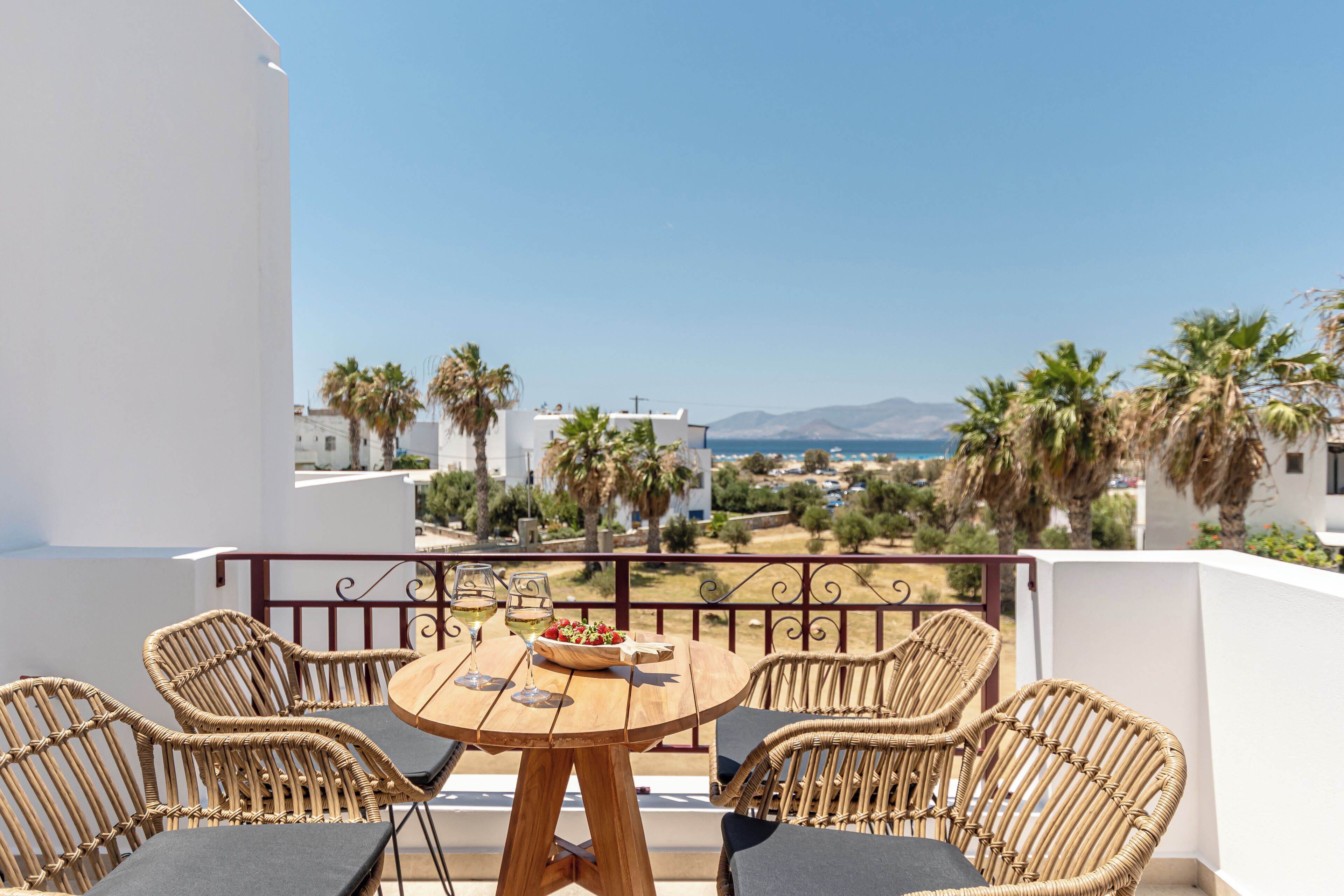 A balcony with wicker furniture, a round table, and a view of the sea and buildings.