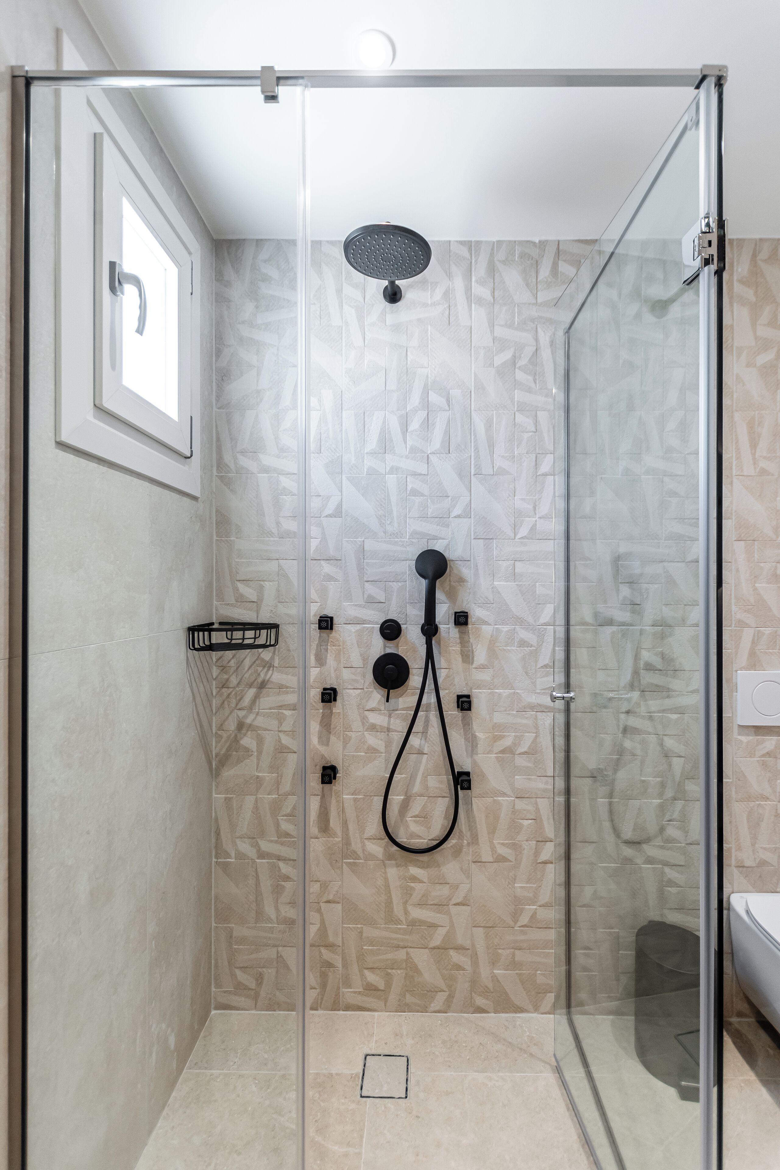Ducha con cerramiento de vidrio, cabezal de ducha manual y toallero negro fijado a la pared.