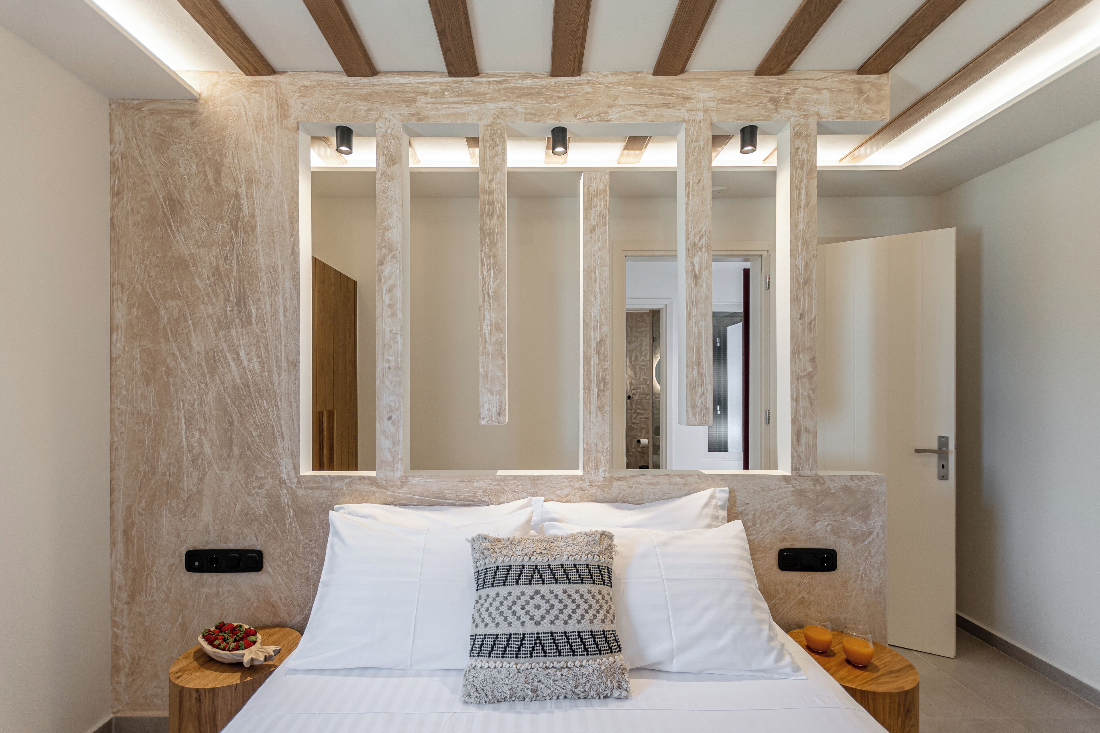 A bedroom with a large bed, a wooden headboard, a mirror, and a bedside table with a bowl of fruit.