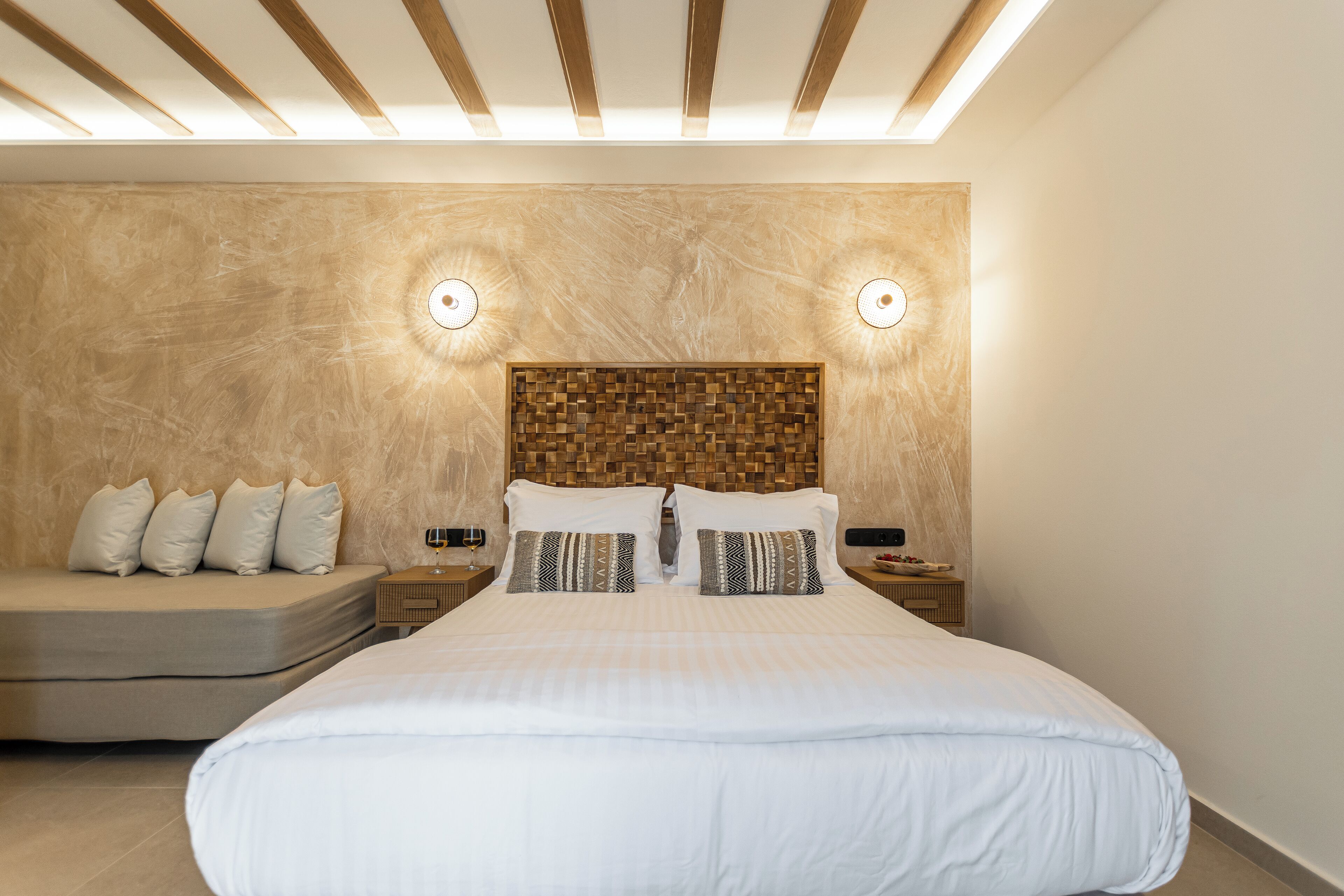 Un dormitorio moderno con una cama grande, un sofá, cabecera de madera y dos mesitas de noche con lámparas.
