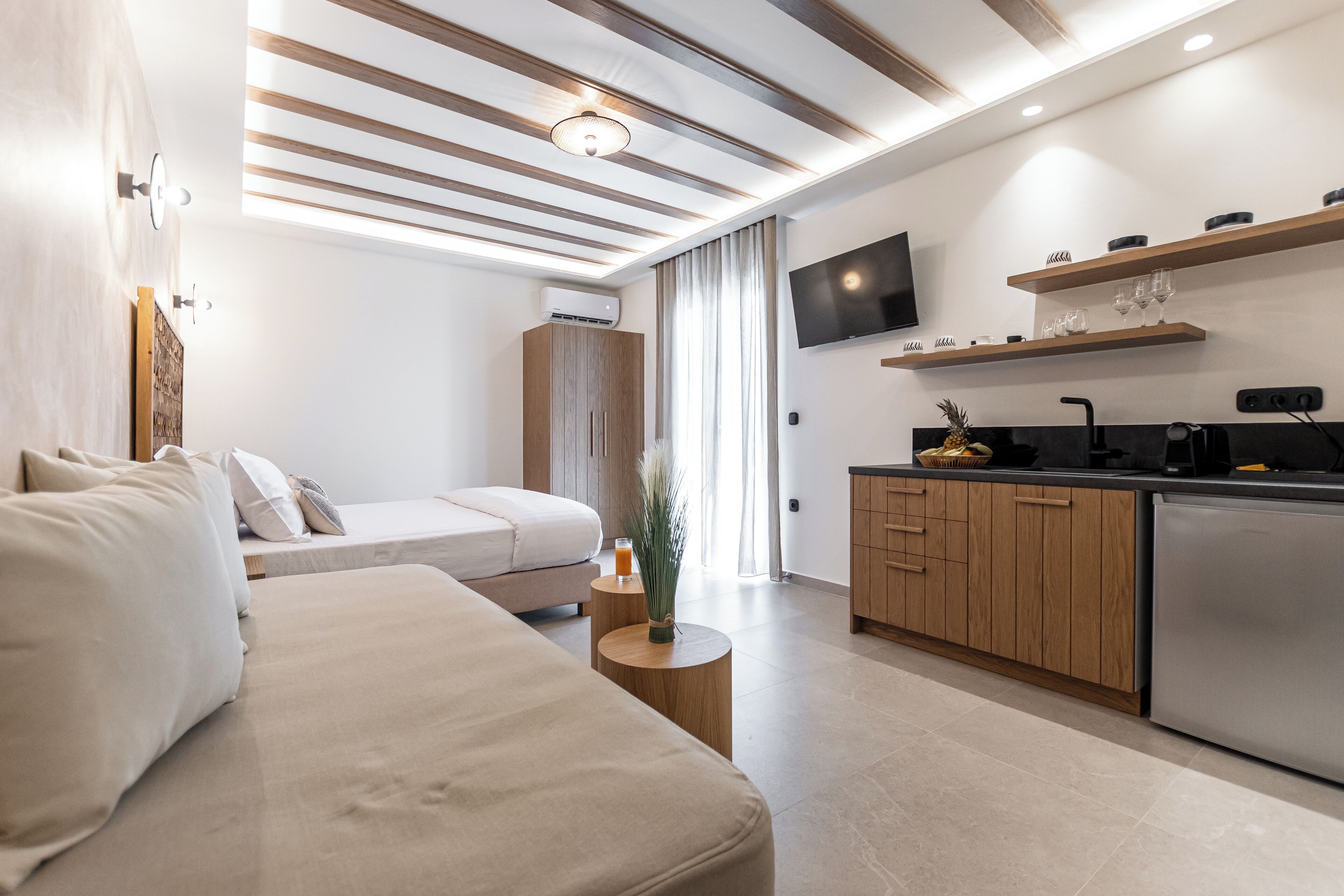 Een moderne hotelkamer met een bed, nachtkastje en een kitchenette met een koelkast, magnetron en een flatscreen televisie aan de muur.