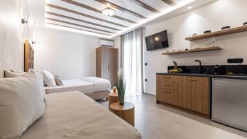 Een moderne hotelkamer met een bed, nachtkastje en een kitchenette met een koelkast, magnetron en een flatscreen televisie aan de muur.