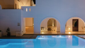 Una piscina con superficie de agua azul cristalina, rodeada de paredes blancas y arcos que dan acceso a un comedor.