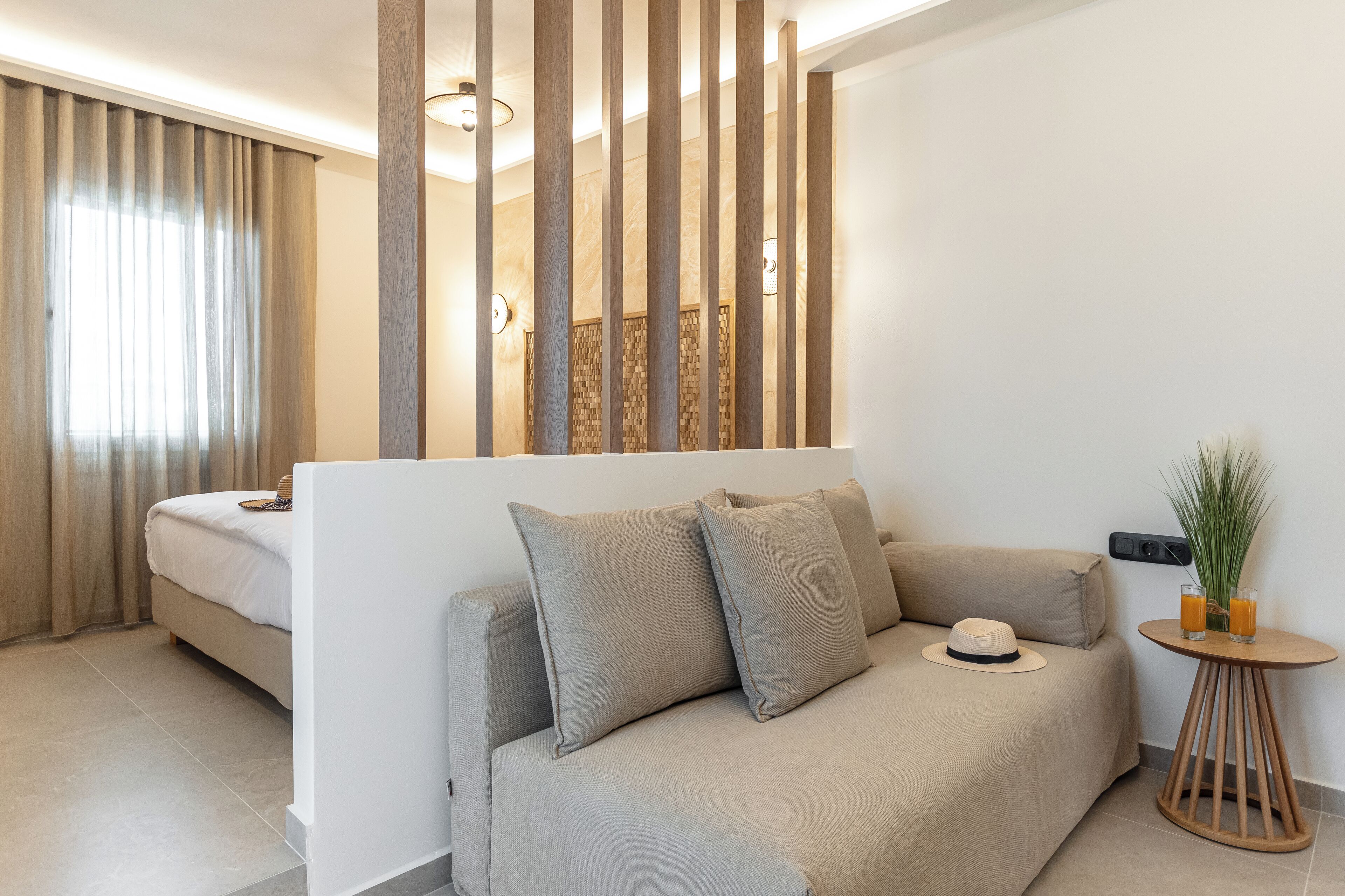 Une chambre d’hôtel moderne avec un canapé, une petite table ronde agrémentée d’un vase et de verres, et un lit avec des rideaux.