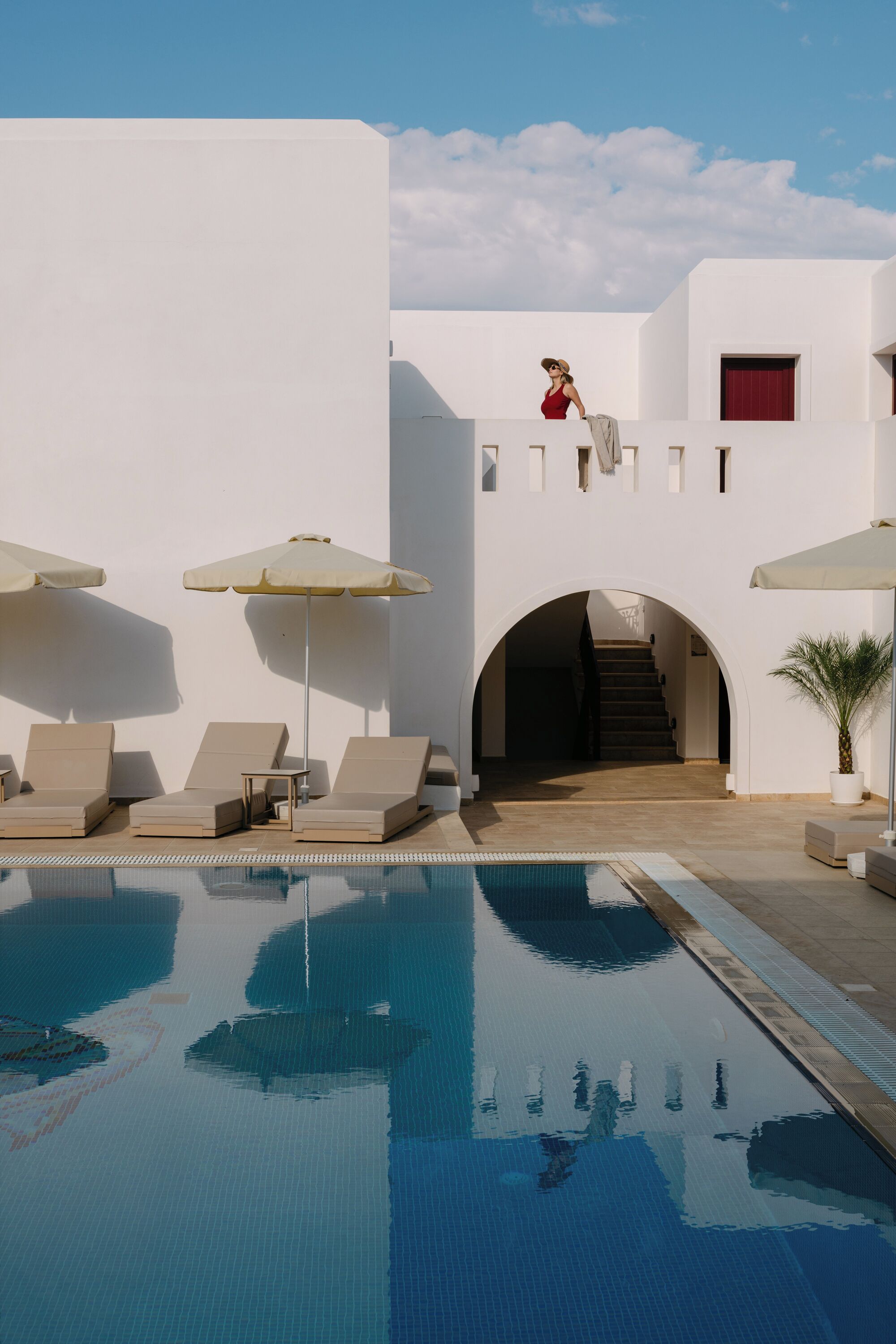 A pool area with lounge chairs and umbrellas, a staircase leading to an upper level, and a clear sky.