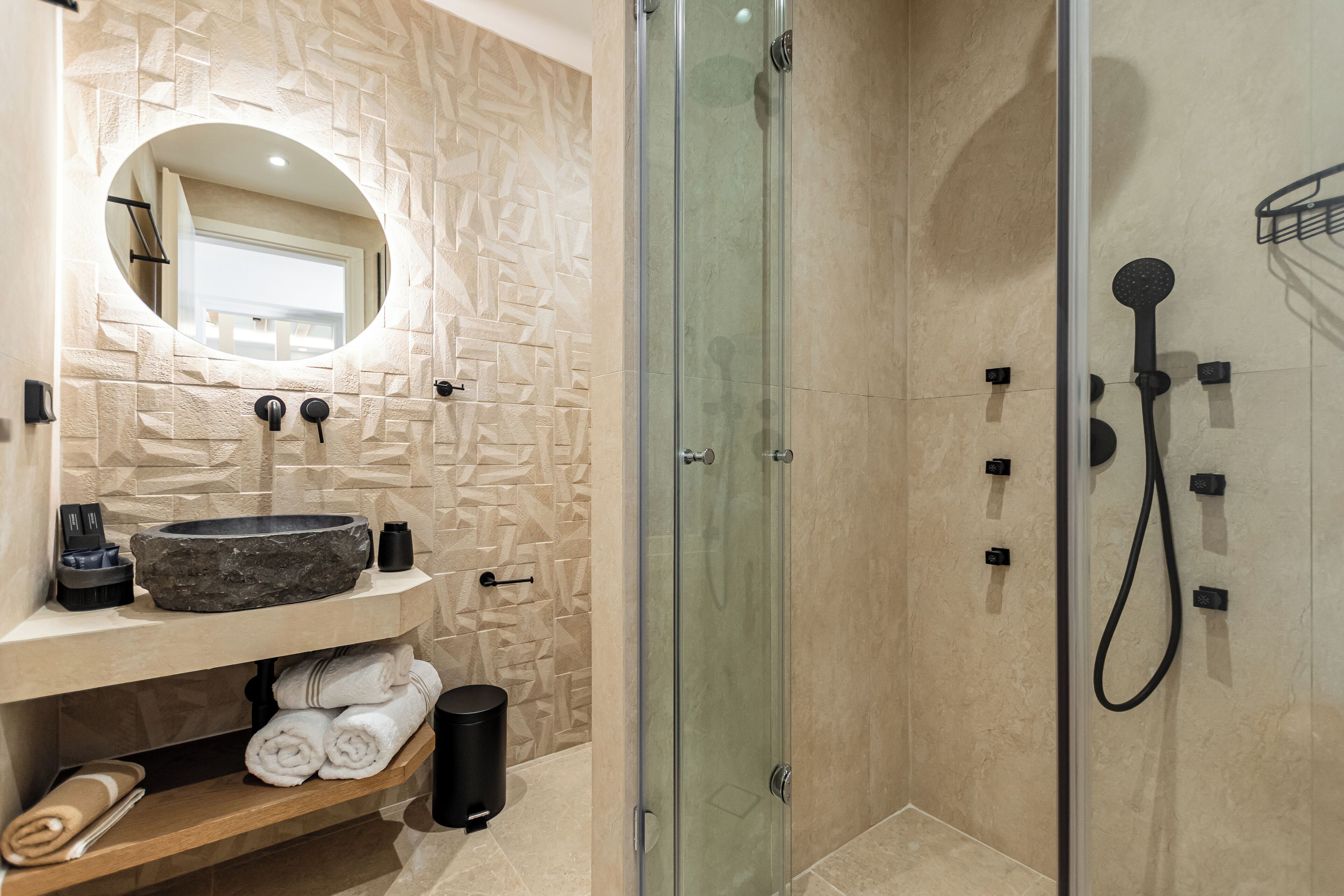 A modern bathroom with a stone sink, a glass shower enclosure, and a built-in mirror.