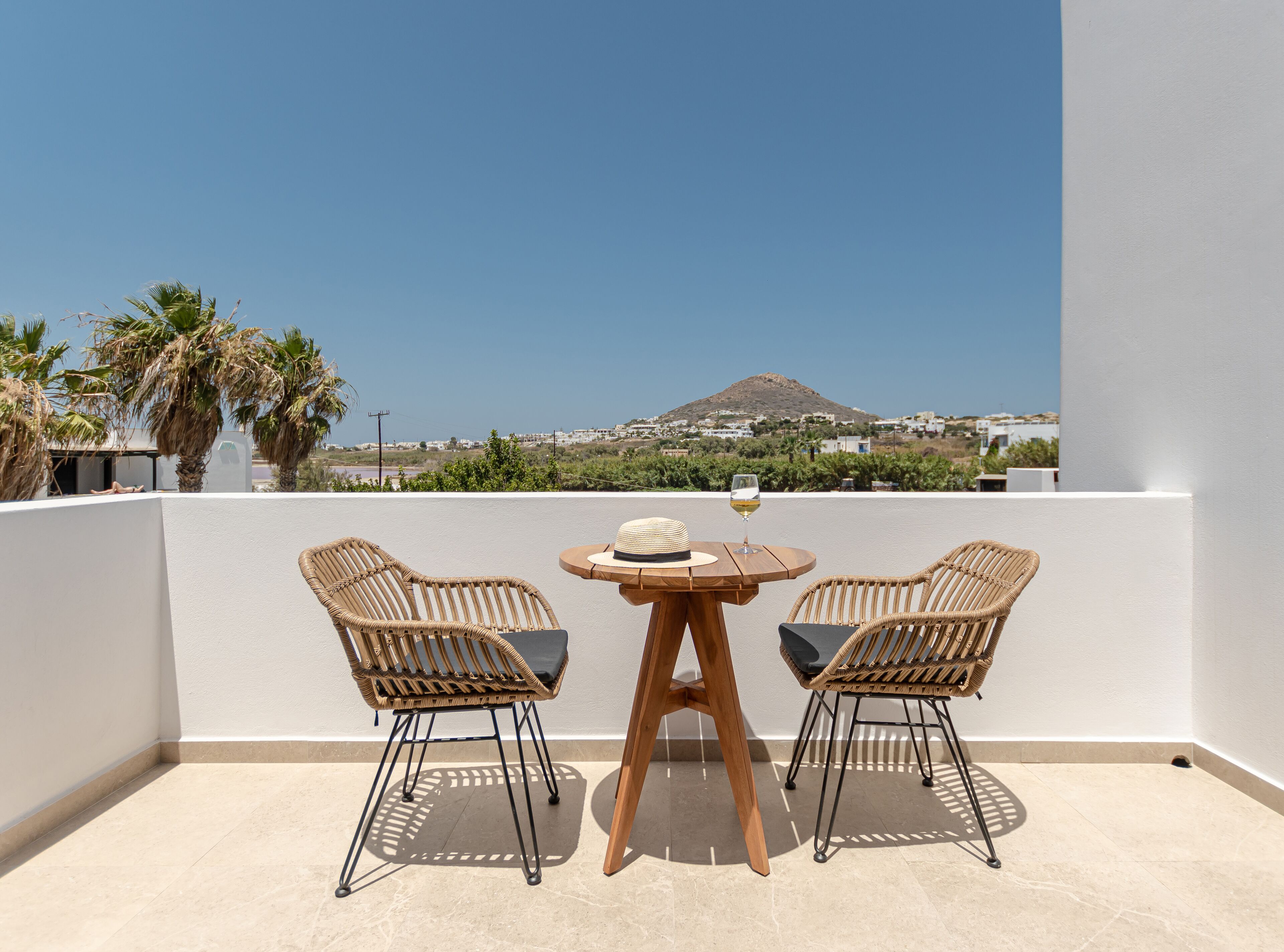 A balcony with two wicker chairs and a small round table, a hat, and a glass of wine.