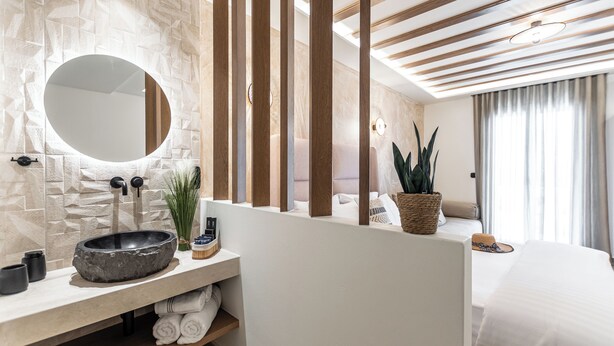 Un baño moderno con pared de piedra, un espejo redondo, un separador de madera, un lavabo con cuenca de piedra y una planta en maceta.