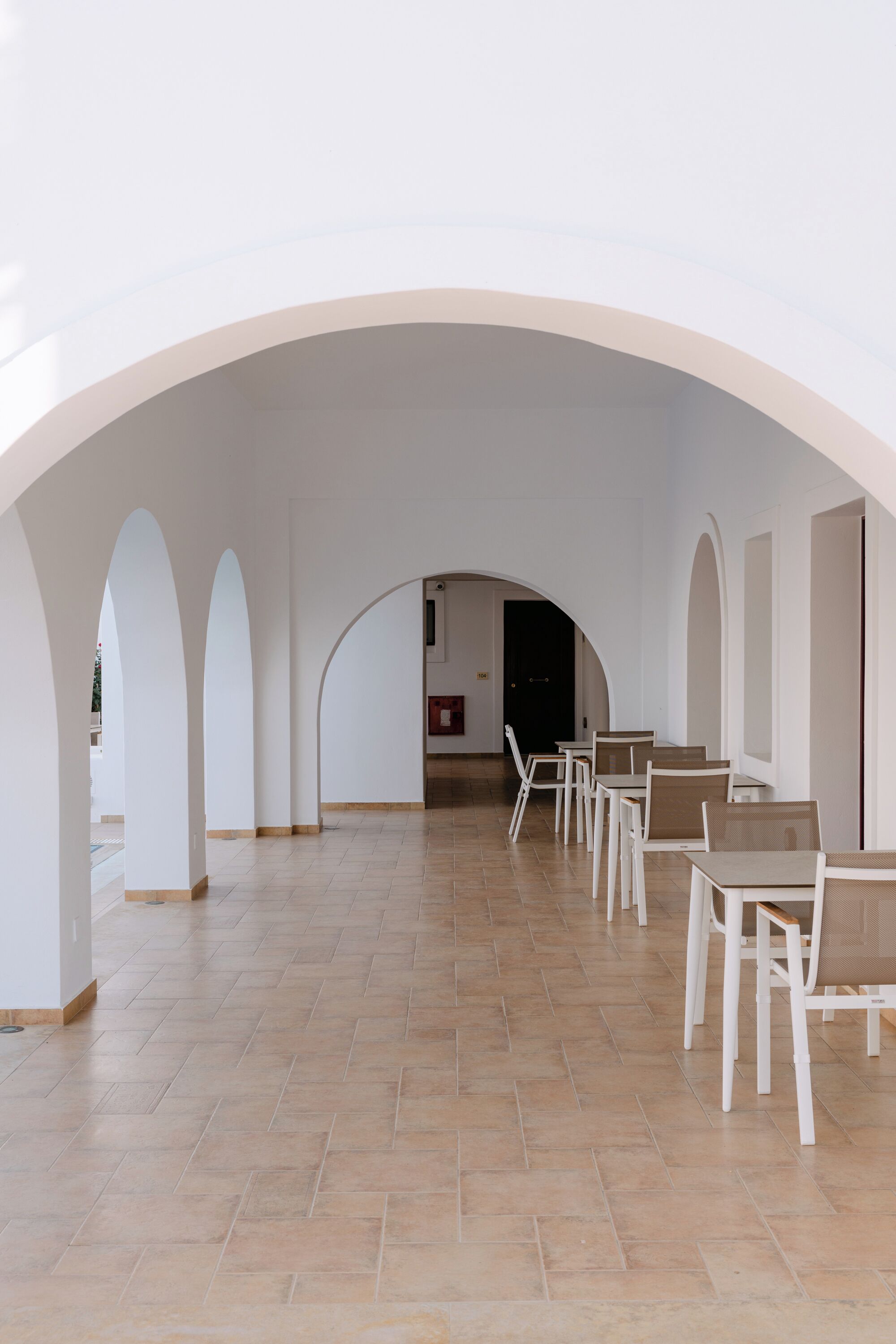 Un vaste espace intérieur agrémenté d’arches blanches, d’un sol carrelé et de plusieurs tables et chaises.