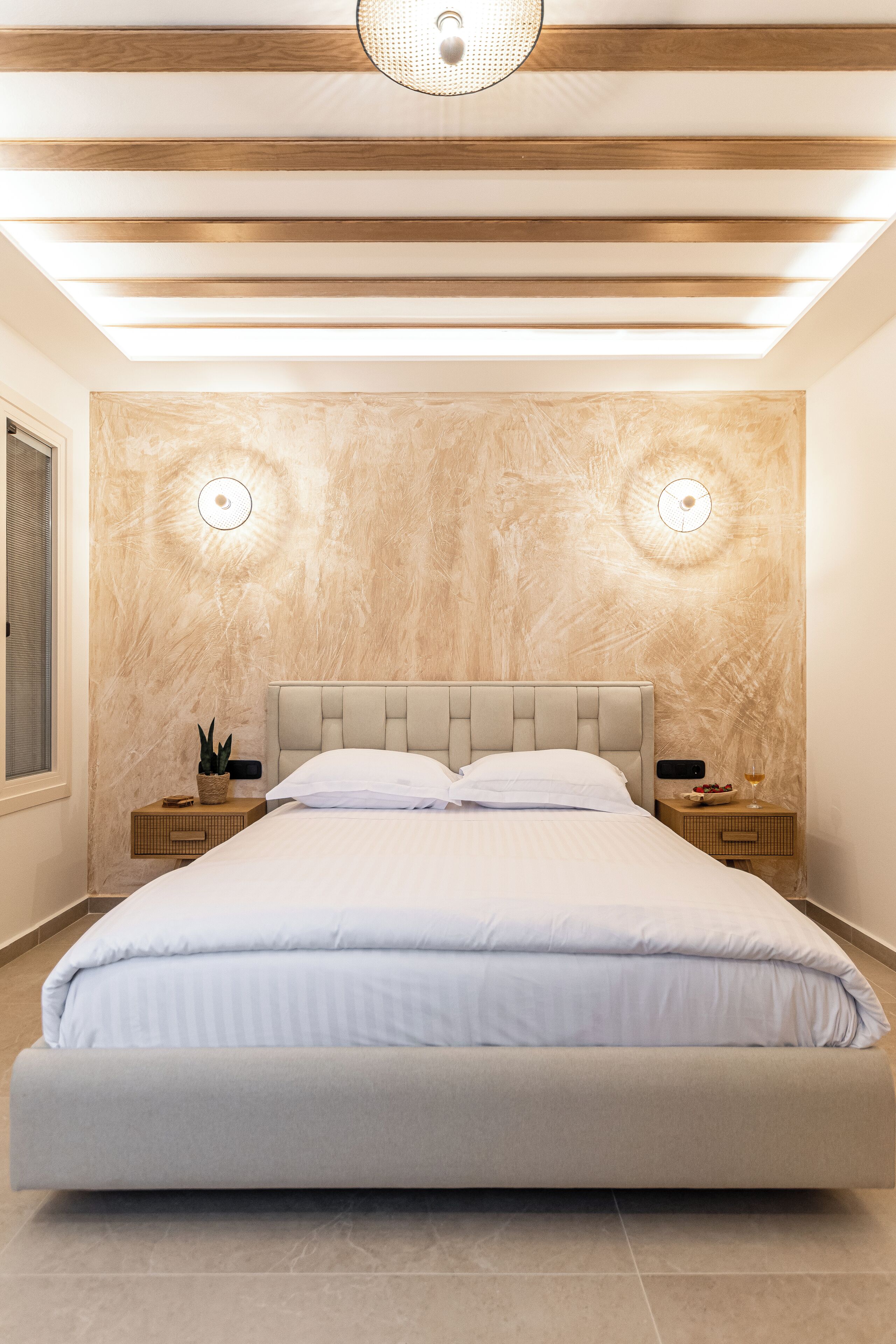 Un dormitorio moderno con una cama grande, vigas de madera en el techo y dos lámparas de pared.