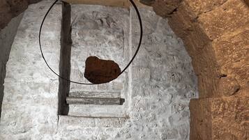 Eine bogenförmige Steinstruktur mit einer kreisförmigen Öffnung oben, einem kleinen rechteckigen Fenster und einem Metallgeländer im Vordergrund.