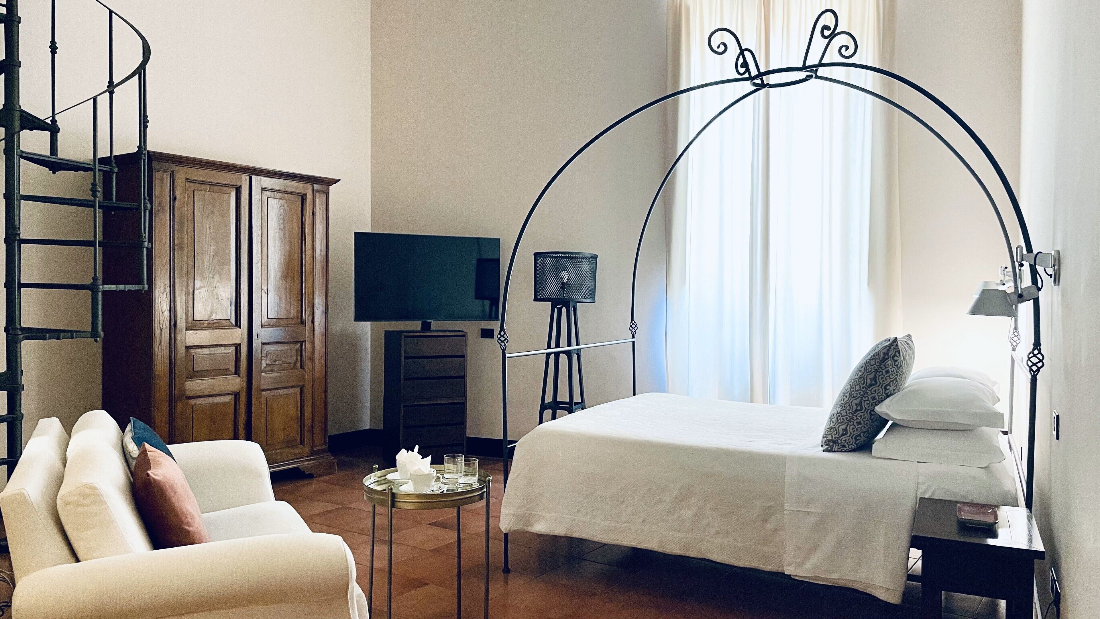 Ein Schlafzimmer mit einem Bett, einem Fernseher, einem Schreibtisch, einem Stuhl, einem Kleiderschrank und einer Wendeltreppe.