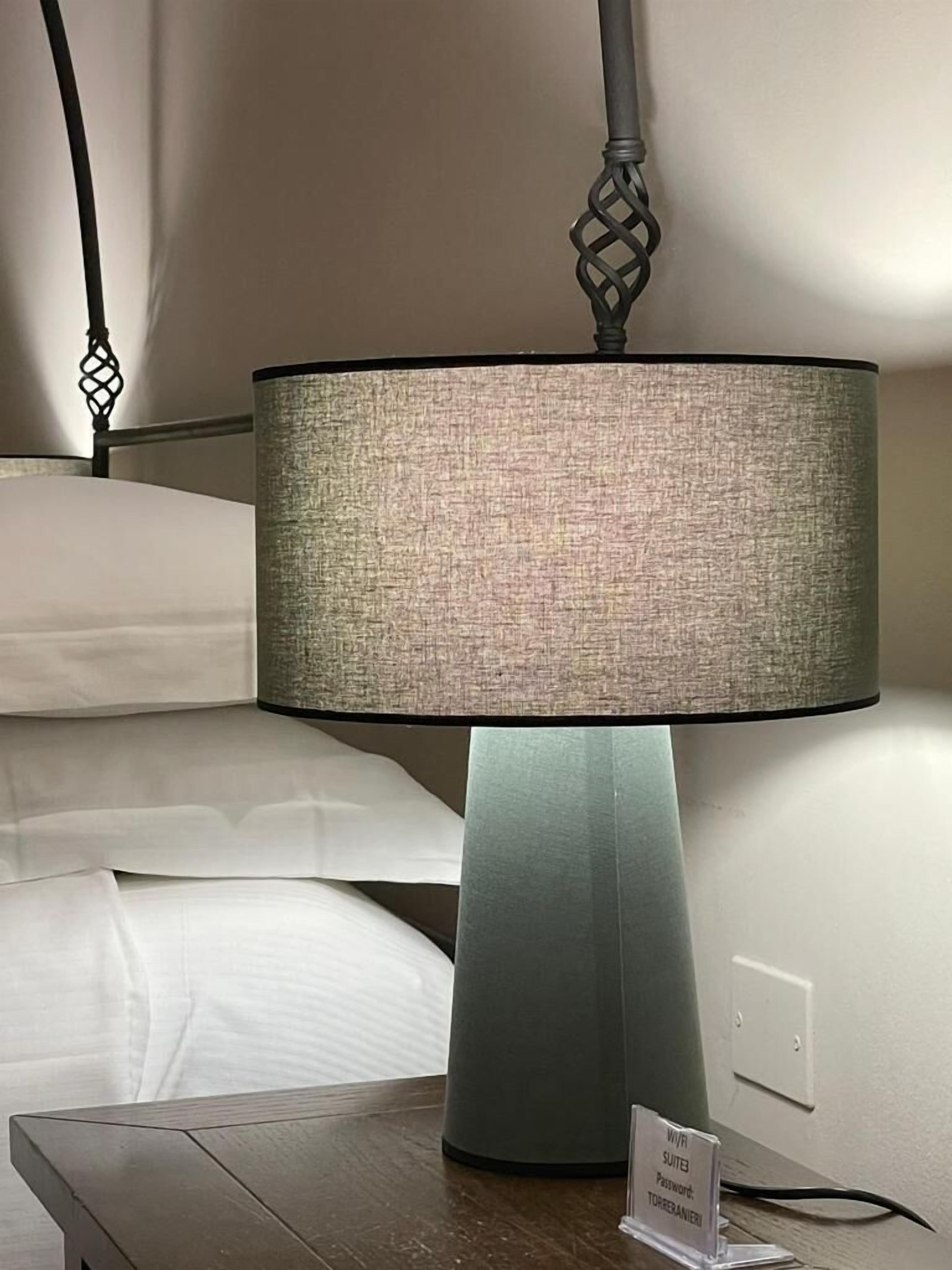 Une table de chevet avec une lampe, un panneau indiquant un mot de passe et une prise électrique au mur.