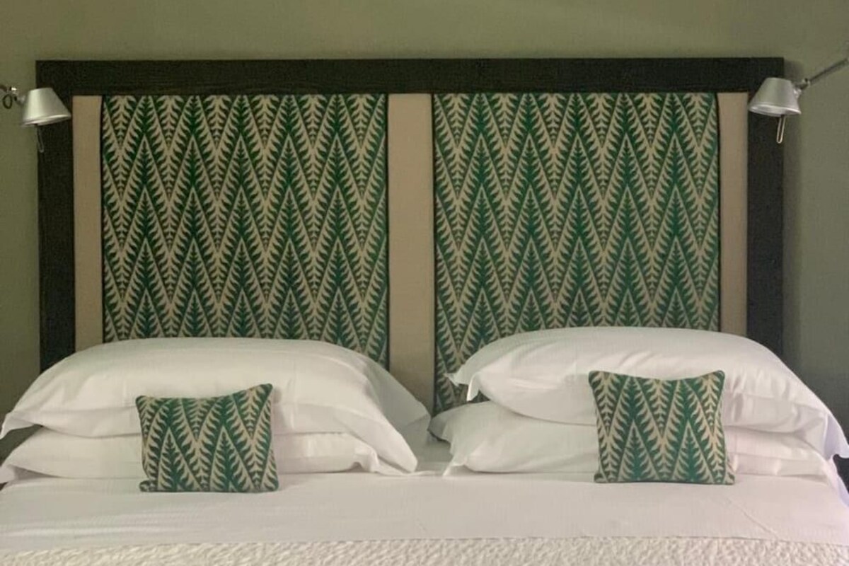 Una cama doble con ropa de cama blanca y dos almohadas, una con estampado de hojas verdes.
