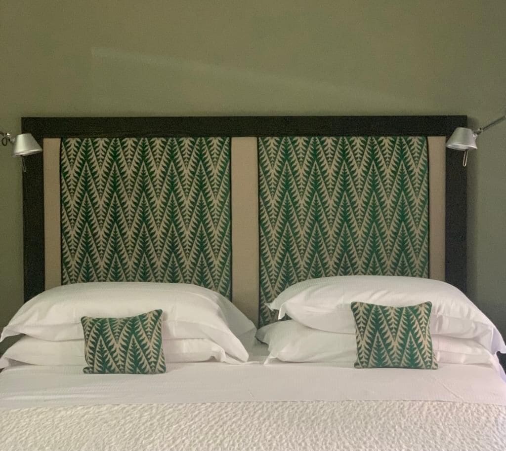 A double bed with white linens and two pillows, one with a green leaf pattern.