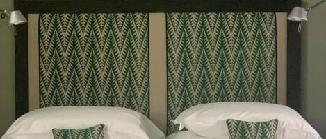 A double bed with white linens and two pillows, one with a green leaf pattern.