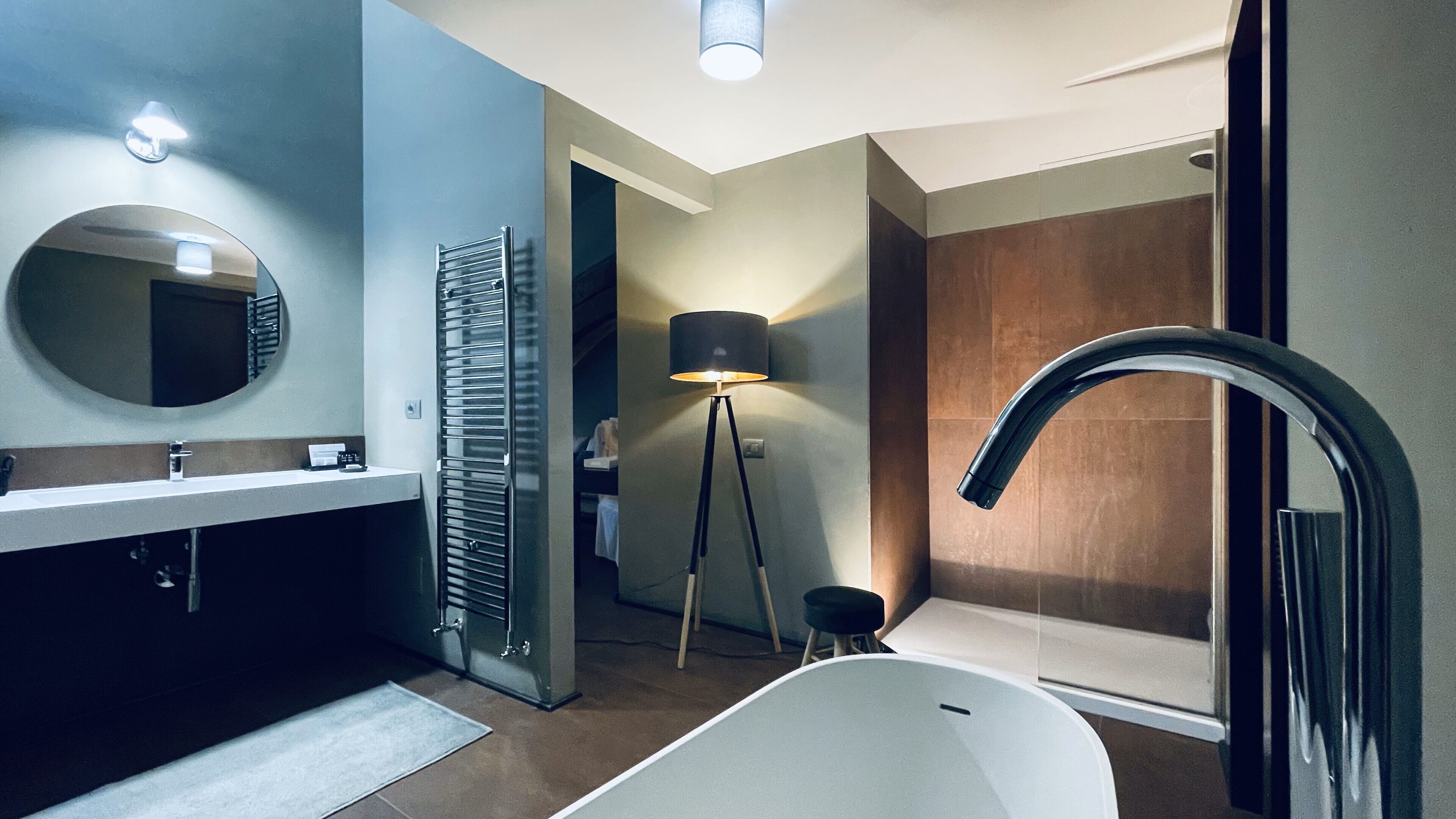 Een moderne badkamer met een bad, een ronde spiegel, een handdoekhouder, een vloerlamp en een douchehoek.