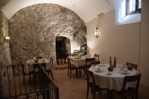 Un espace de restauration aux murs de pierre, avec des tables dressées pour le repas, un escalier et une vue sur le mur de pierre.