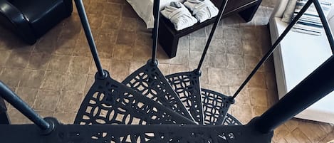 A spiral staircase with a geometric metal design, leading to a bedroom with a bed, bedside tables, and a lamp.