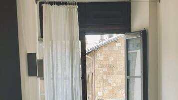 Un baño con una bañera independiente, una ventana que ofrece vistas a un edificio de ladrillo y una silla.