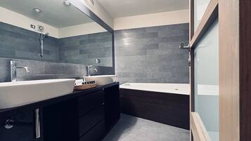 Un baño moderno con dos lavamanos, una bañera y muebles de madera oscura.