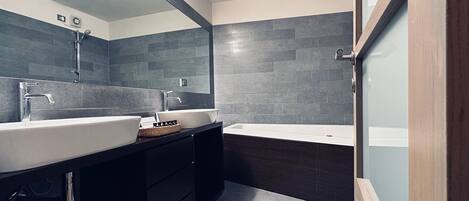 Un baño moderno con dos lavamanos, una bañera y muebles de madera oscura.