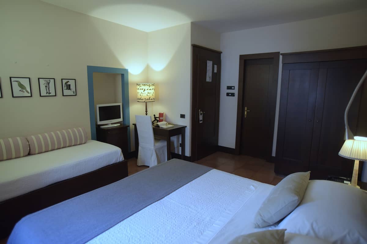 Ein Hotelzimmer mit Bett, Schlafsofa, Schreibtisch mit Stuhl, Lampe und Kleiderschrank.