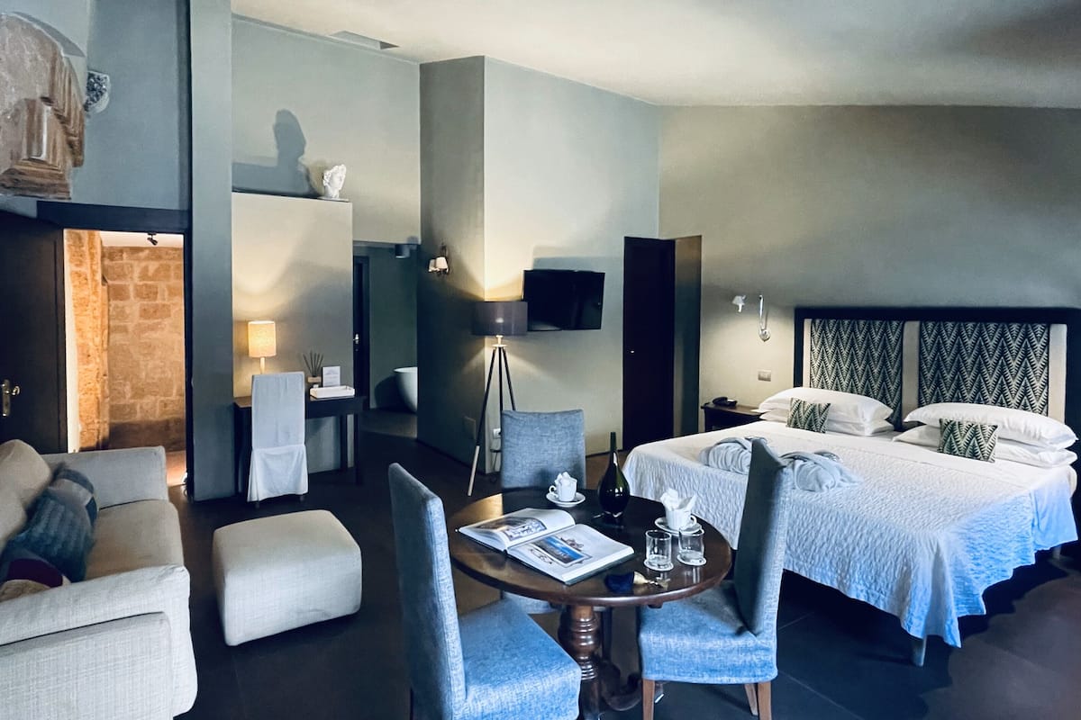Ein Hotelzimmer mit Bett, Schreibtisch, Sessel, Sofa und Fernseher.