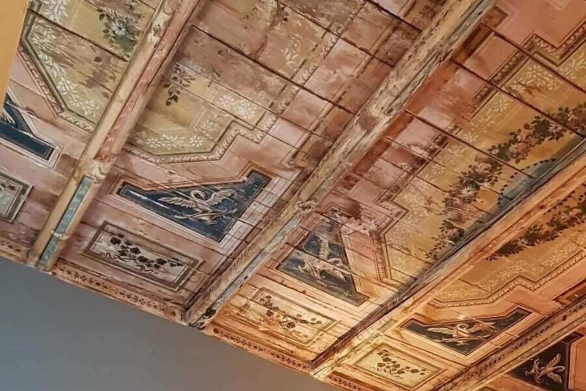 Ein Zimmer mit einem Bett, einer kunstvoll gestalteten Decke und einer Leuchte.