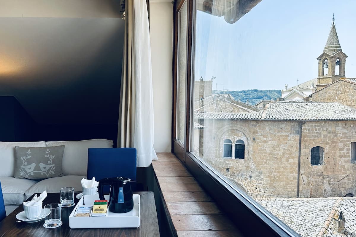 Ein Hotelzimmer mit Blick auf ein historisches Gebäude, eine Sitzecke, ein Tisch mit einem Frühstücksangebot und eine Lampe.