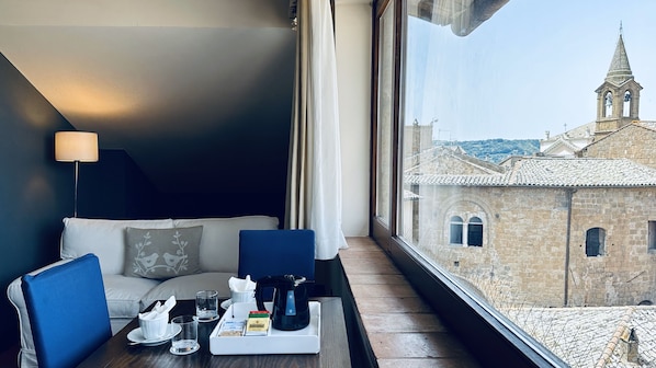 Une chambre d’hôtel avec vue sur un bâtiment historique, un canapé, une table avec un plateau de petit-déjeuner et une lampe.