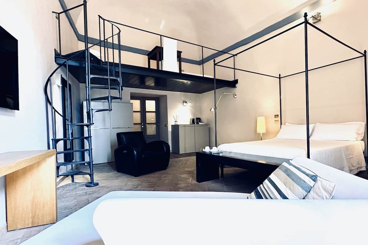 Ein Schlafzimmer mit Himmelbett, Schreibtisch, Stuhl, Nachttischchen, Lampe, Kleiderschrank, Spiegel und einer Treppe.