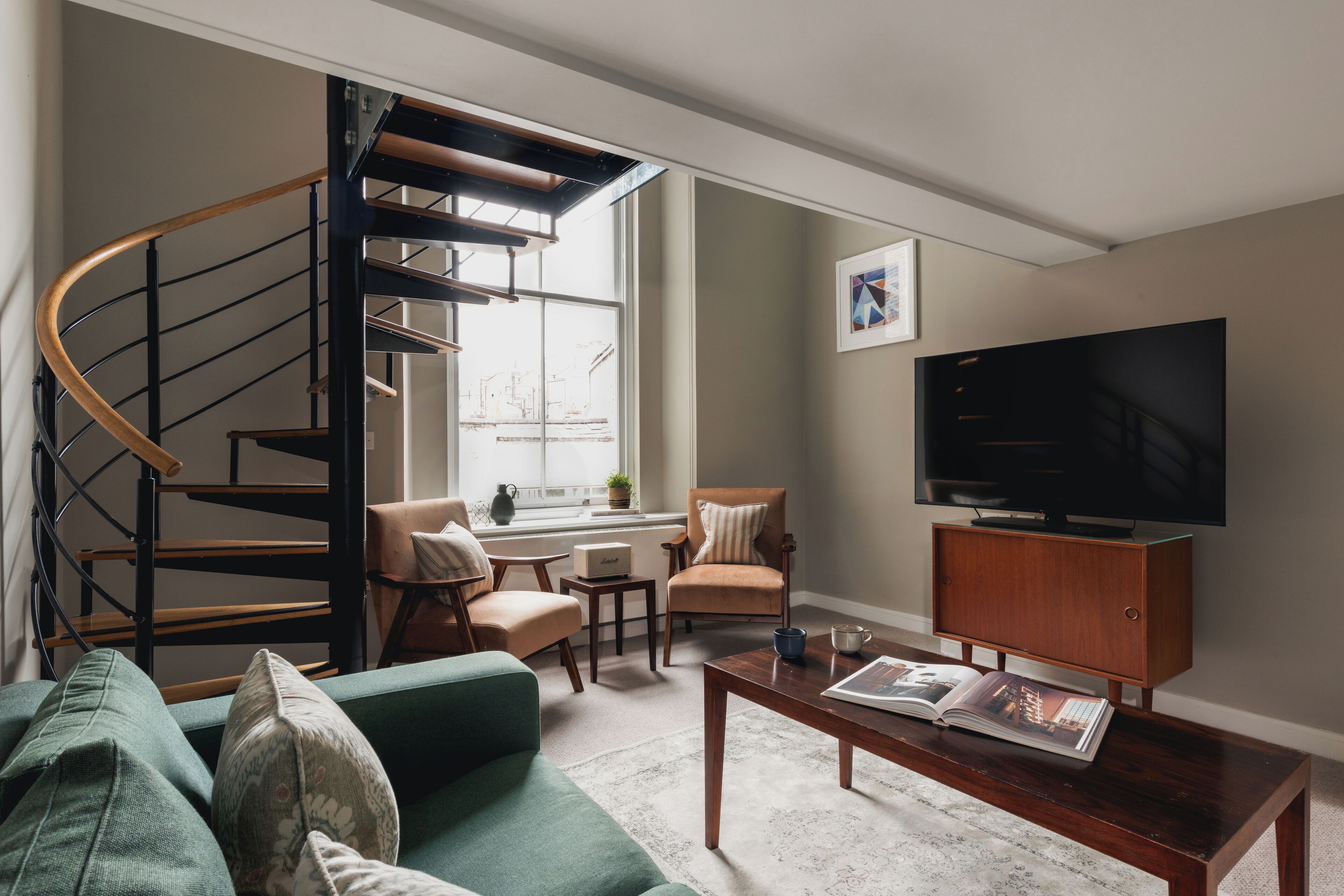 A modern living room with a spiral staircase, a green sofa, a wooden coffee table, and a television.