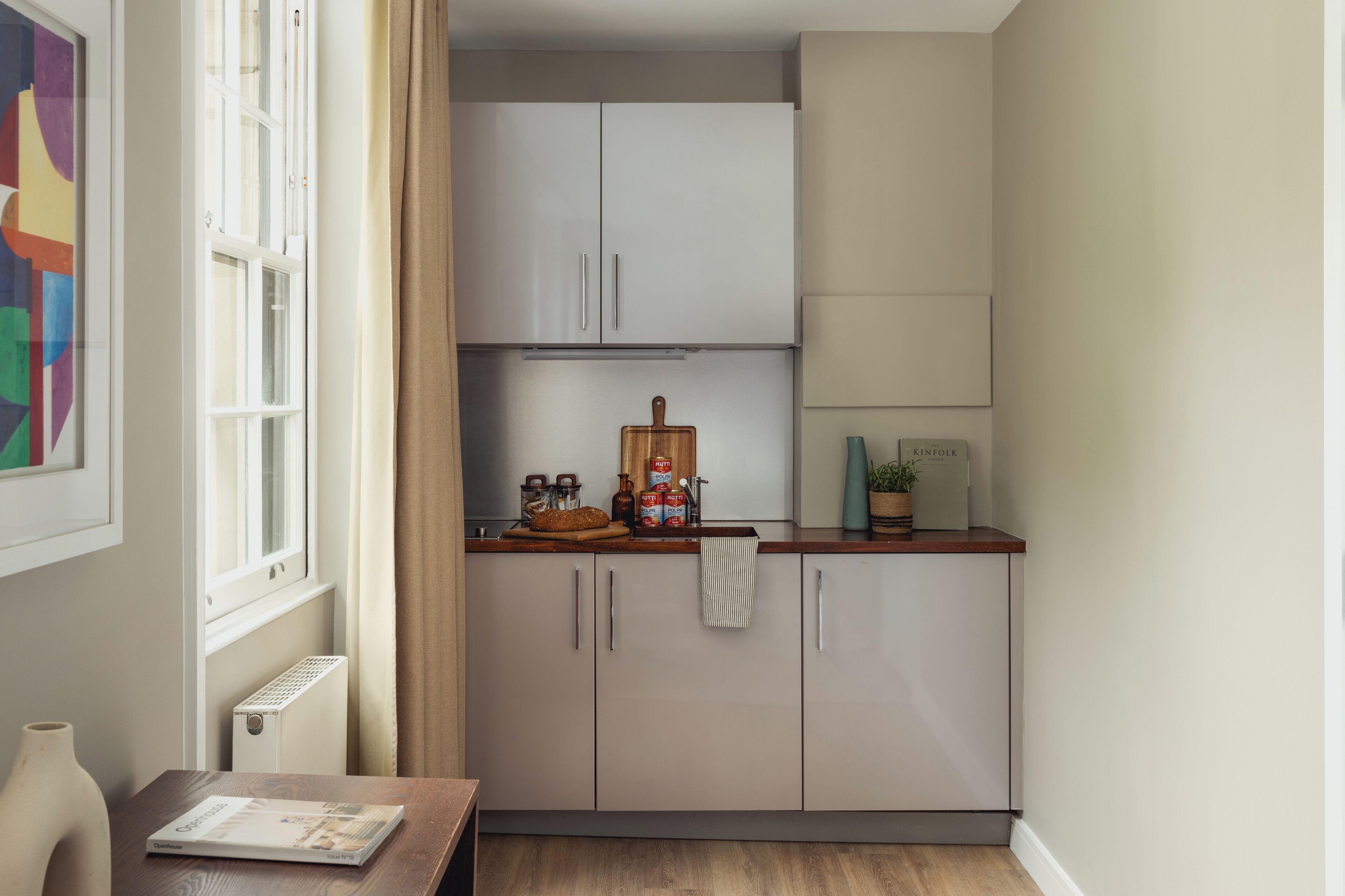 A compact kitchen with light-colored cabinets, a wooden countertop, and a window with curtains.