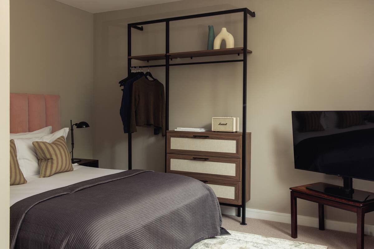 Un dormitorio con cama, televisor, cómoda y estantería.