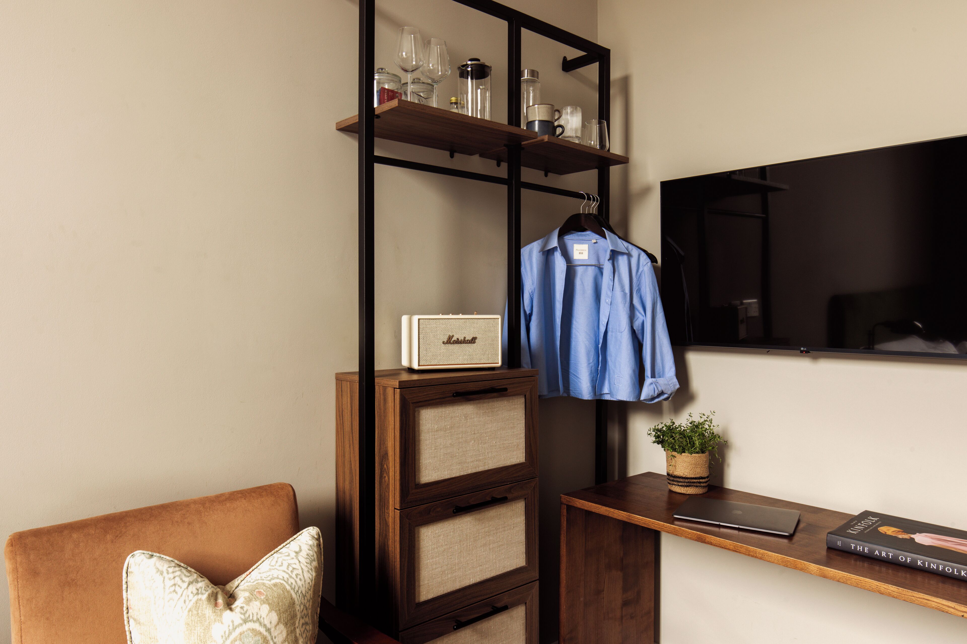 Ein Zimmer mit einem Holztisch, einem blauen Hemd an einem Kleiderbügel, einer kleinen Pflanze und einem Buch mit dem Titel "The Art of Kinfolk".