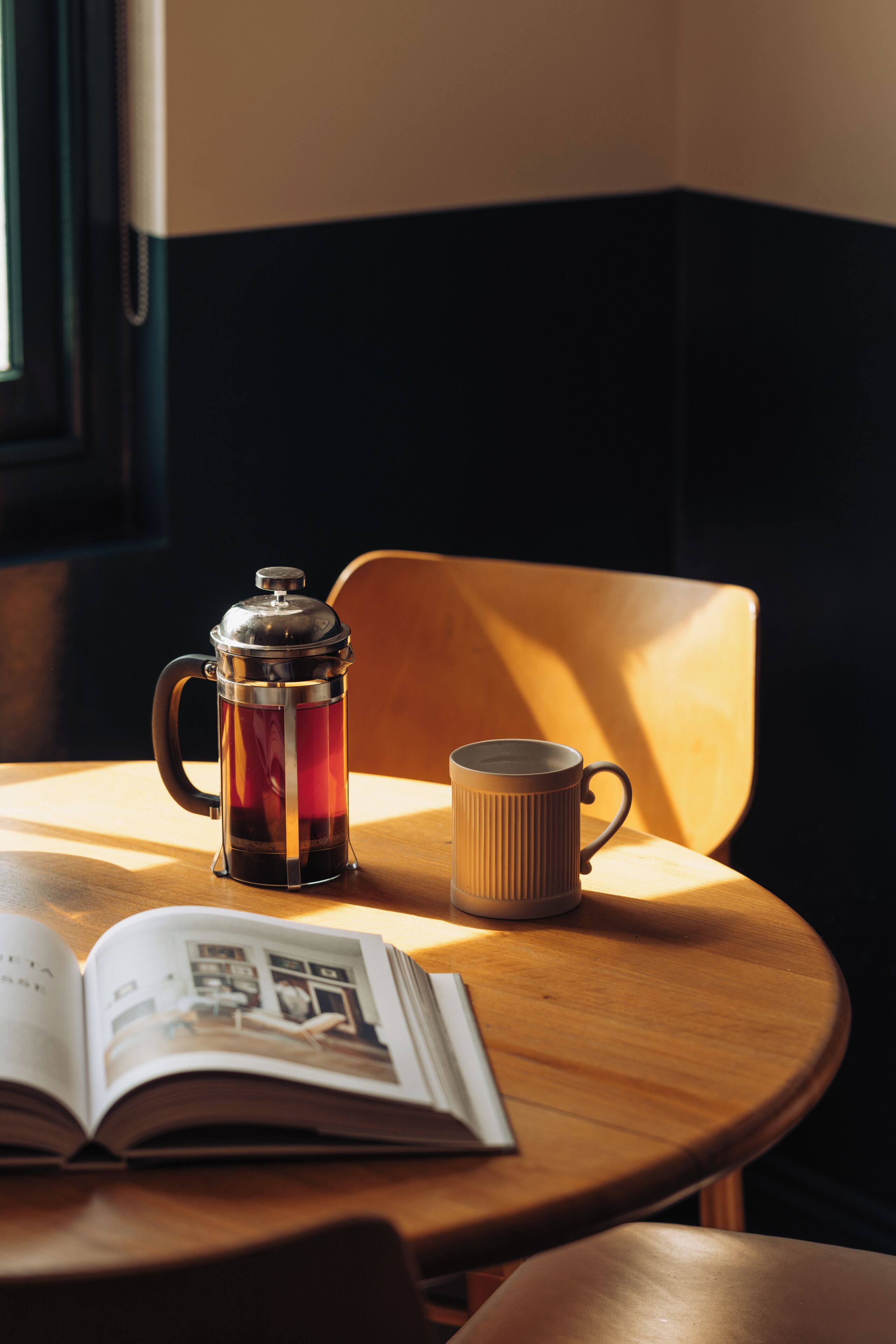 Een koffiezetapparaat en mok op een houten tafel met een open boek.