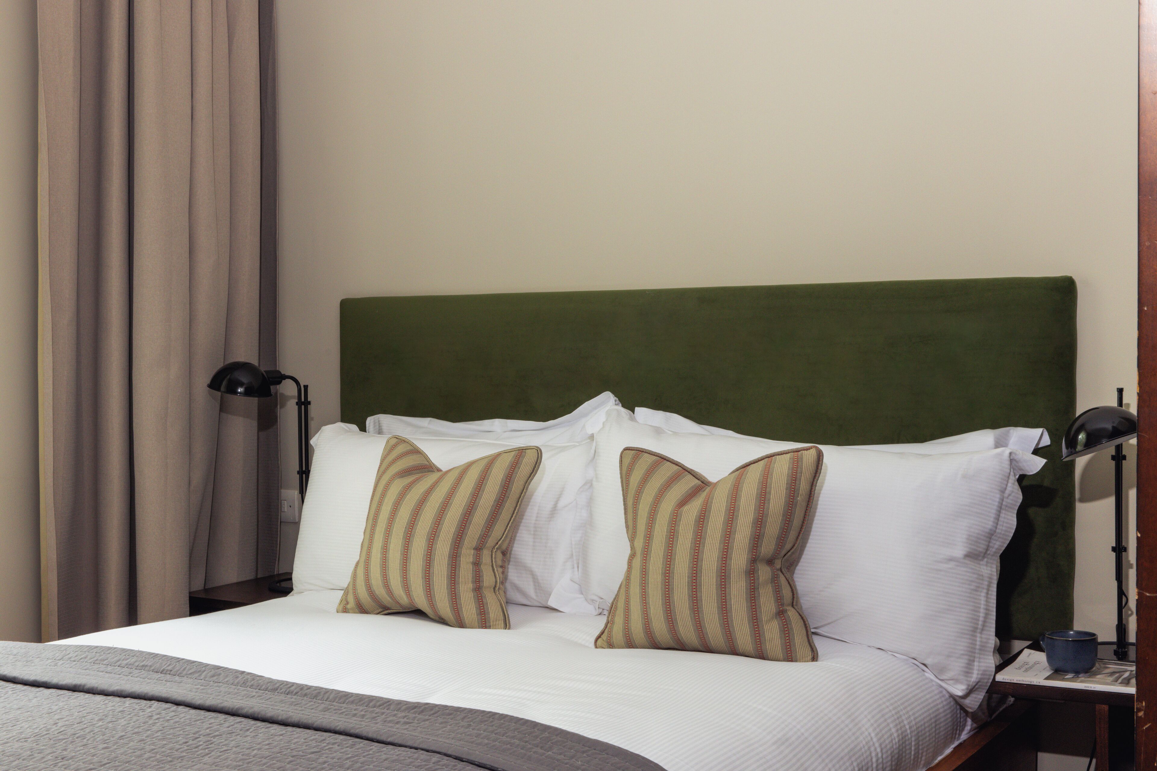 A neatly made bed with white and striped pillows, a green headboard, and a lamp on a bedside table.