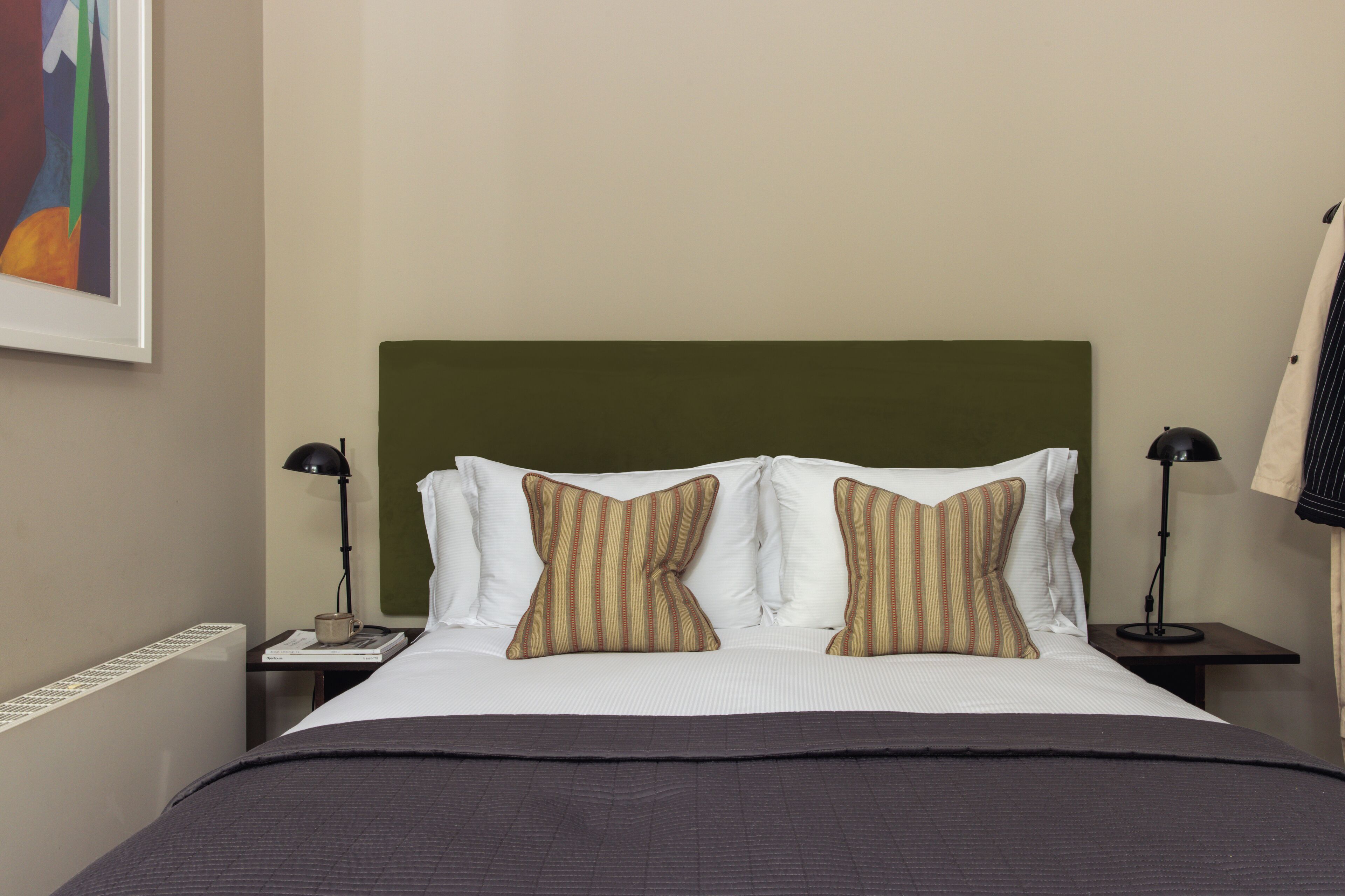 A neatly made bed with striped pillows, a green headboard, and two bedside lamps.